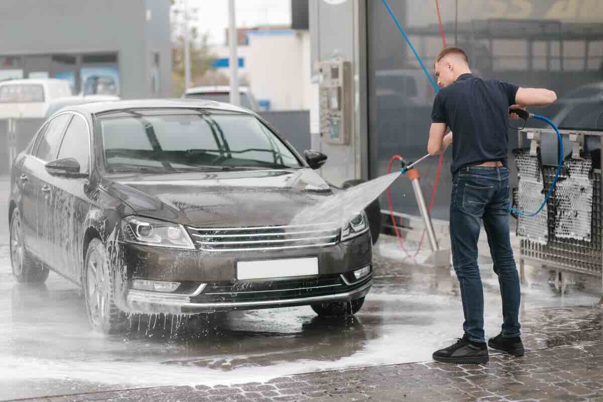 uomo con maglia nera che lava auto nera con idropulitrice