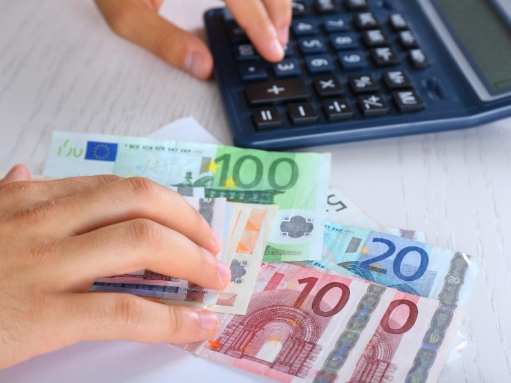 Banconote euro e persona che fa i calcoli con calcolatrice