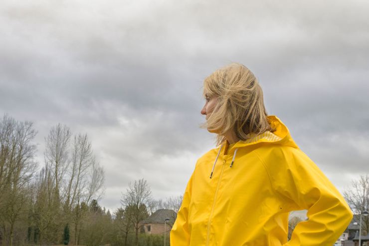 Ragazza con un impermeabile giallo, al parco. Il tempo è nuvoloso.