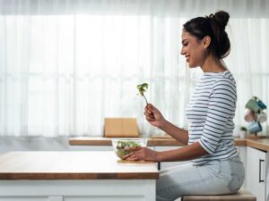 donna seduta e felice che mangia insalata con forchetta