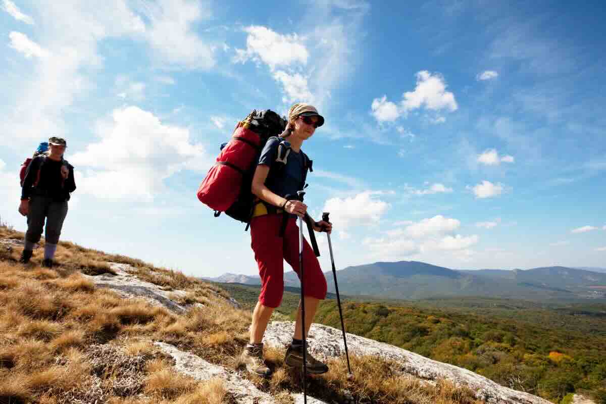 Donna con zaino in spalla e bastoni percorre sentiero di un cammino