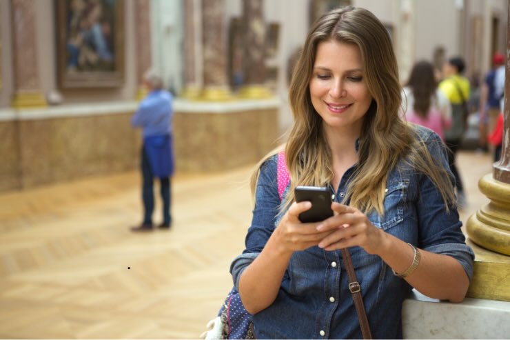 ragazza con smartphone che sorride dentro un museo