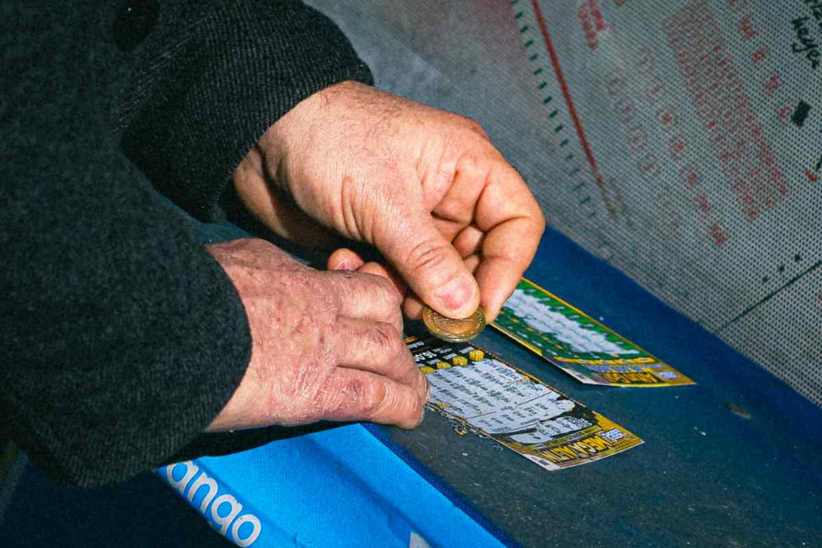 uomo che con una moneta gratta i biglietti della lotteria