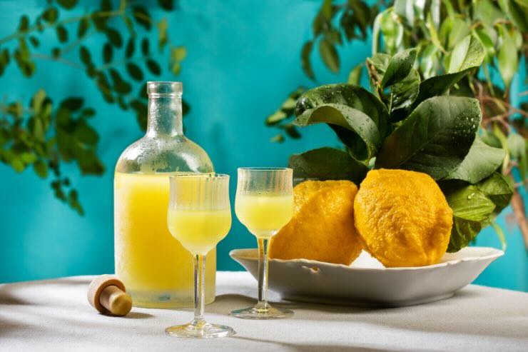 Bottiglia con limoncello, due bicchieri con limoncello e due limoni 